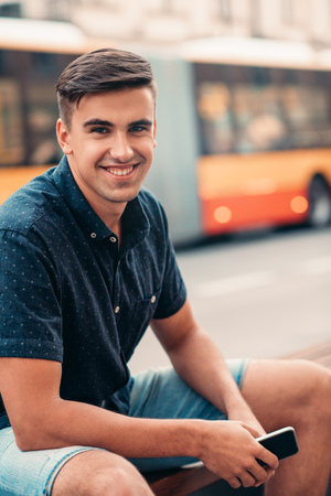 Smiling young man sitting on a bench in the cityの写真素材