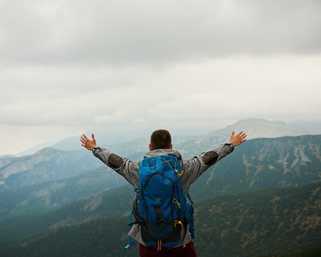 Rearview of a man in hiking gear with arms raised to the sky embracing the view from a mountain peak while trekking in the wildernessの写真素材