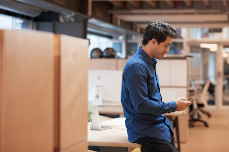 Young businessman standing in an office sending a text messageの写真素材