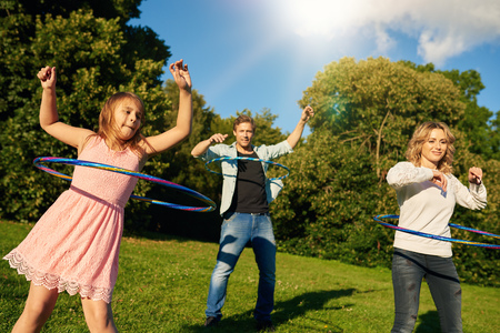 Happy family of three playing with hula hoops while enjoying a day in a park together on a sunny summer dayの写真素材
