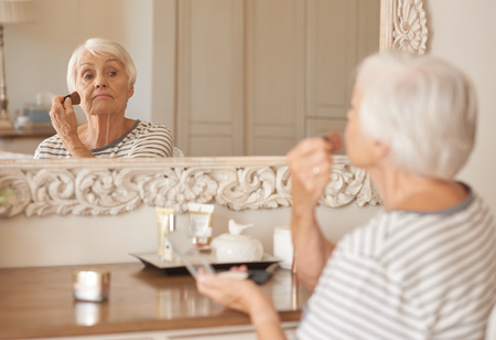 Senior woman applying makeup to her cheek in a mirrorの写真素材