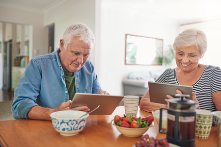 Smiling seniors using digital tablets over breakfast at homeの写真素材