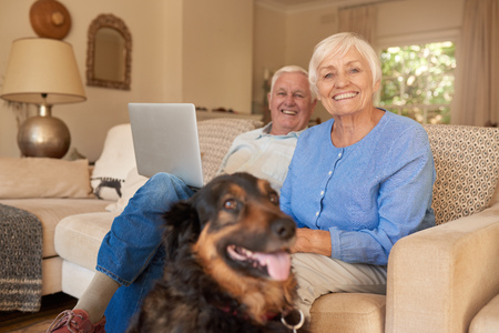 Smiling senior couple relaxing with their dog at homeの写真素材