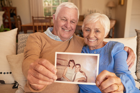 Smiling senior couple holding a photo of their youthful selvesの写真素材