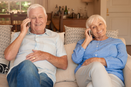 Content senior couple sitting and talking on cellphones at homeの写真素材