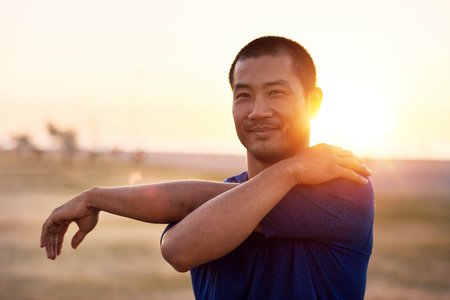 Fit young Asian man stretching his arms before a runの写真素材