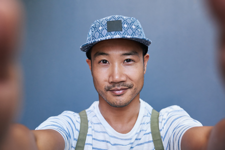 Smiling young Asian man taking a selfie outsideの写真素材