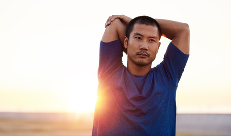 Fit Asian man stretching his shoulders before a morning runの写真素材
