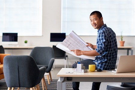 Confident Asian architect reading blueprints in an officeの写真素材