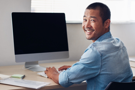 Happy young Asian entrepreneur at work on an office computerの写真素材
