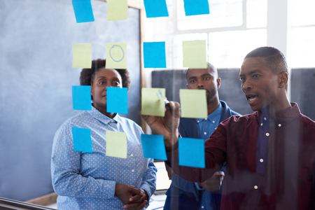 African businesspeople brainstorming with sticky notes on a glass wall