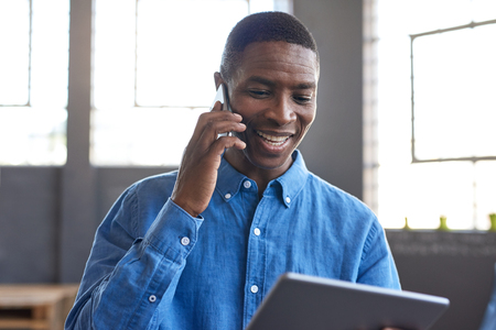 Smiling African businessman using a tablet and cellphone at workの写真素材