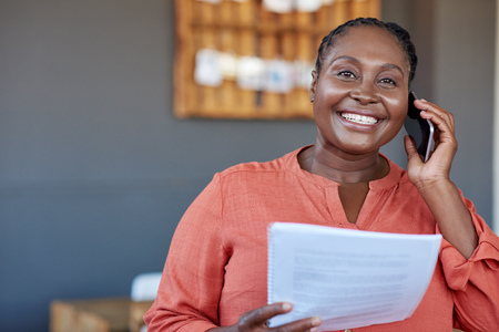 African businesswoman using a cellphone and reading documents at workの写真素材