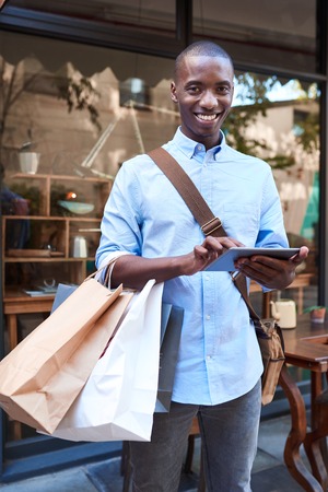 Young man using a tablet while shopping in the cityの写真素材