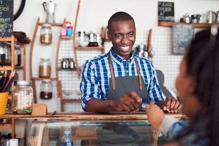 Smiling barista taking a credit card from a cafe customerの写真素材