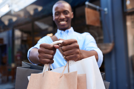 Smiling man standing outside carrying a load of shopping bagsの写真素材