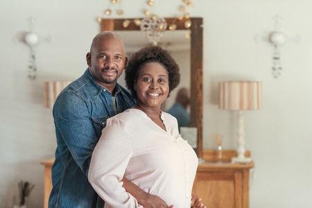 Smiling African couple standing affectionately together in their living roomの写真素材