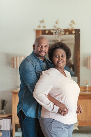 Smiling African couple standing lovingly together in their living roomの写真素材