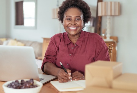 Smiling African woman writing in a notebook and working online