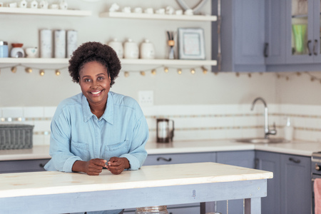 Smiling young African woman leaning on her kitchen islandの写真素材