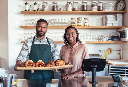 Smiling African entrepreneurs with baked goods behind their bakery counterの写真素材