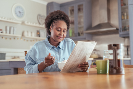 Young woman reading the newspaper while eating breakfast at homeの写真素材