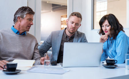 Three focused businesspeople using a laptop together in an office