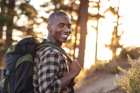 Smiling young African man hiking along a trail at duskの写真素材