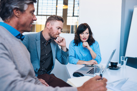 Focused businesspeople working on a laptop together in an officeの写真素材