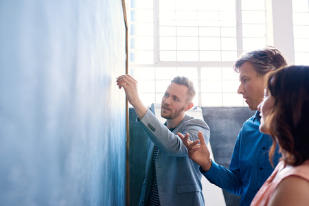 Three colleagues brainstorming on a chalkboard in an officeの写真素材