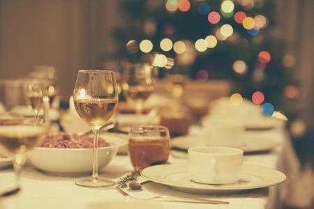 Dining table full of a variety of delicious festive food and wine with a Christmas tree in the background in home with vintage moodの写真素材