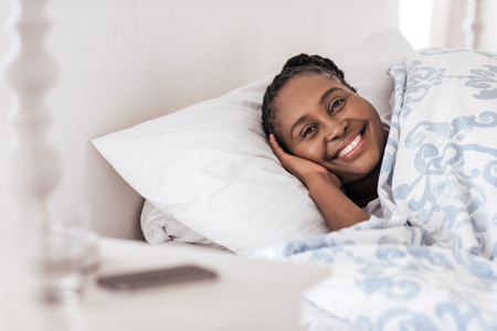 Smiling young African woman waking up in her bedの写真素材