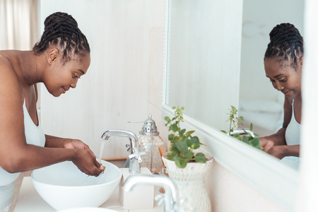 Young African woman washing her face in the bathroom sinkの写真素材