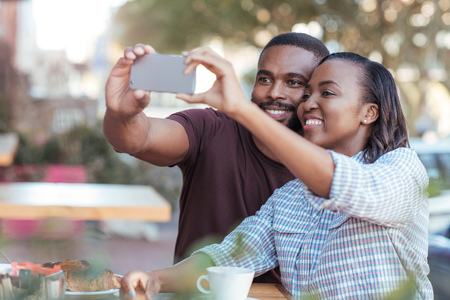 Young African couple taking selfies at a sidewalk cafeの写真素材