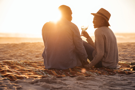 Young African couple watching a beach sunset and drinking wineの写真素材