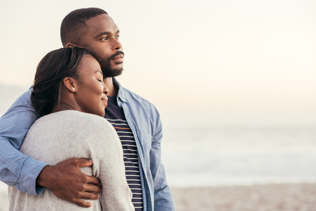 Smiling young African couple enjoying a sunset at the beachの写真素材