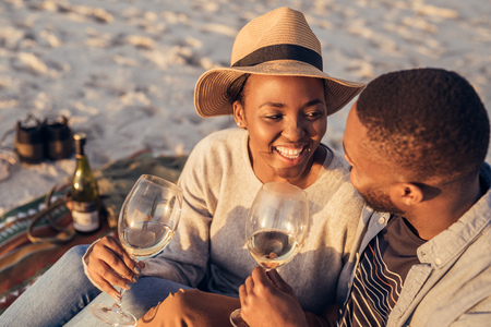 Happy young African couple drinking wine together at the beachの写真素材