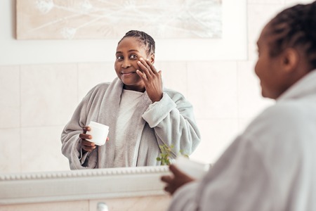 Young African woman applying face cream in the bathroomの写真素材