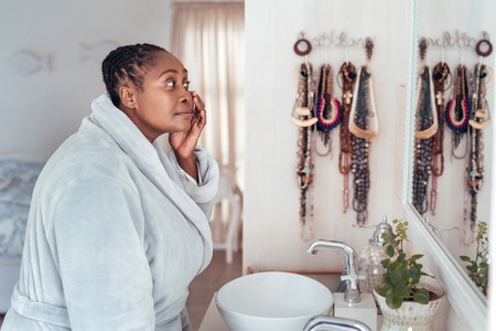 African woman looking at her face in a bathroom mirrorの写真素材
