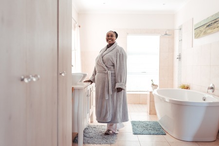 Smiling African woman wearing a robe standing in her bathroomの写真素材