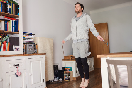 Young man in sportswear jumping rope in his living roomの写真素材