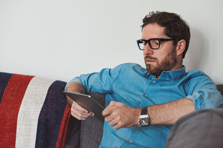 Young man sitting on his sofa using a digital tabletの写真素材
