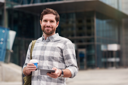 Smiling man using a tablet while walking in the cityの写真素材