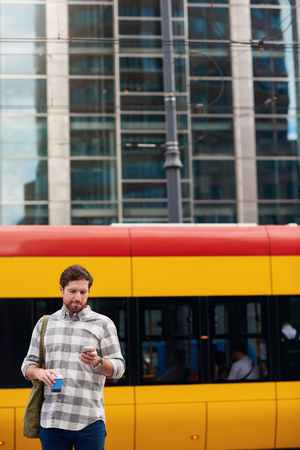 Young man reading messages while standing at a bus stopの写真素材