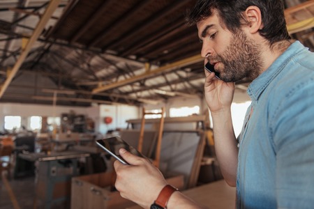 Young carpenter standing in his workshop talking over the phone