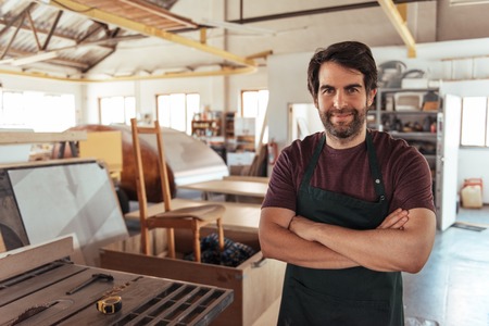 Smiling woodworker standing by a bench saw in his workshopの写真素材