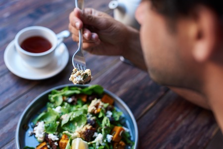 Man eating delicious salad while sitting at a bistro tableの写真素材