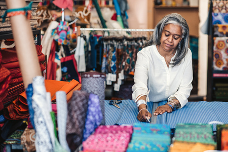 Mature woman marking cloth in her fabric shop before cuttingの写真素材