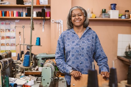 Smiling mature seamstress standing in her sewing workshopの写真素材