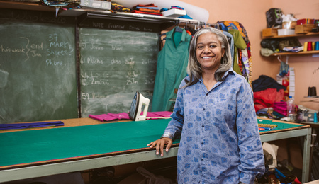 Smiling mature seamstress standing in her dressmaking workshopの写真素材